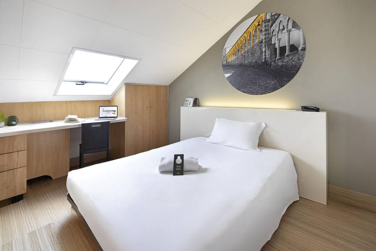 Une chambre d’hôtel équipée d’un lit, d’un bureau, d ’un ordinateur et ornée d’une grande œuvre d’art circulaire au mur.