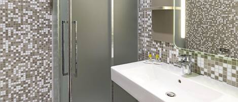 Un baño con cabina de ducha de vidrio, un lavamanos blanco y un salpicadero de azulejos.