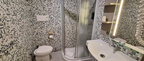 A bathroom with a shower, toilet, and sink, featuring mosaic tile walls and floor.