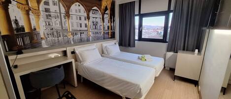 A hotel room with two beds, a desk, a chair, a TV, and a window with a view.