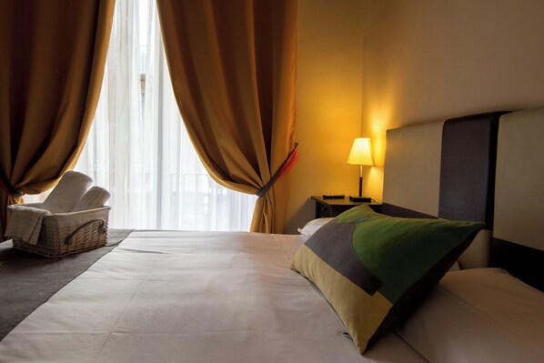 A hotel room with a bed, a chair, a lamp, and a window with curtains. - Hotel Plebiscito Aparthotel (Naples)