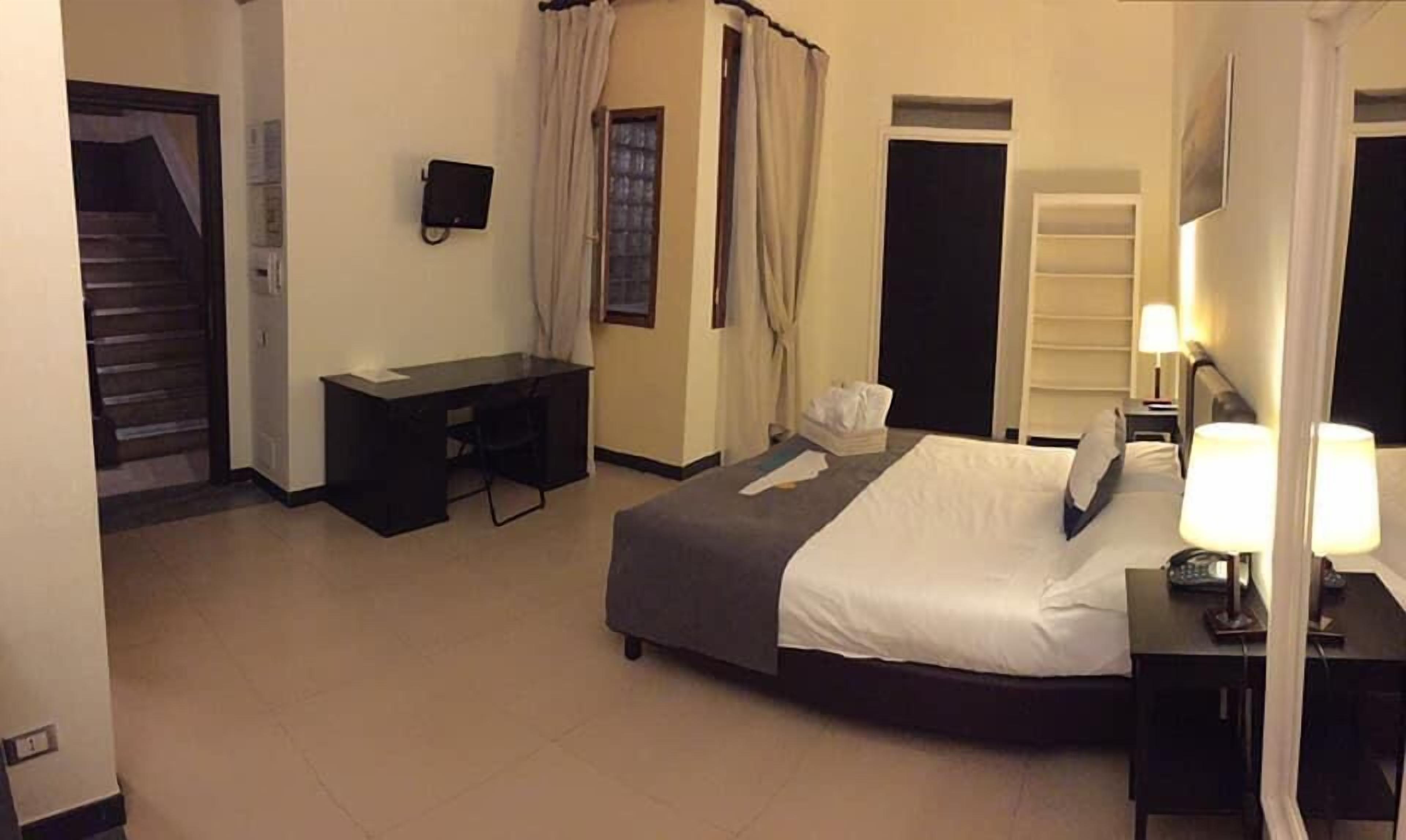 A hotel room with a bed, desk, chair, bedside lamps, and a window with curtains.