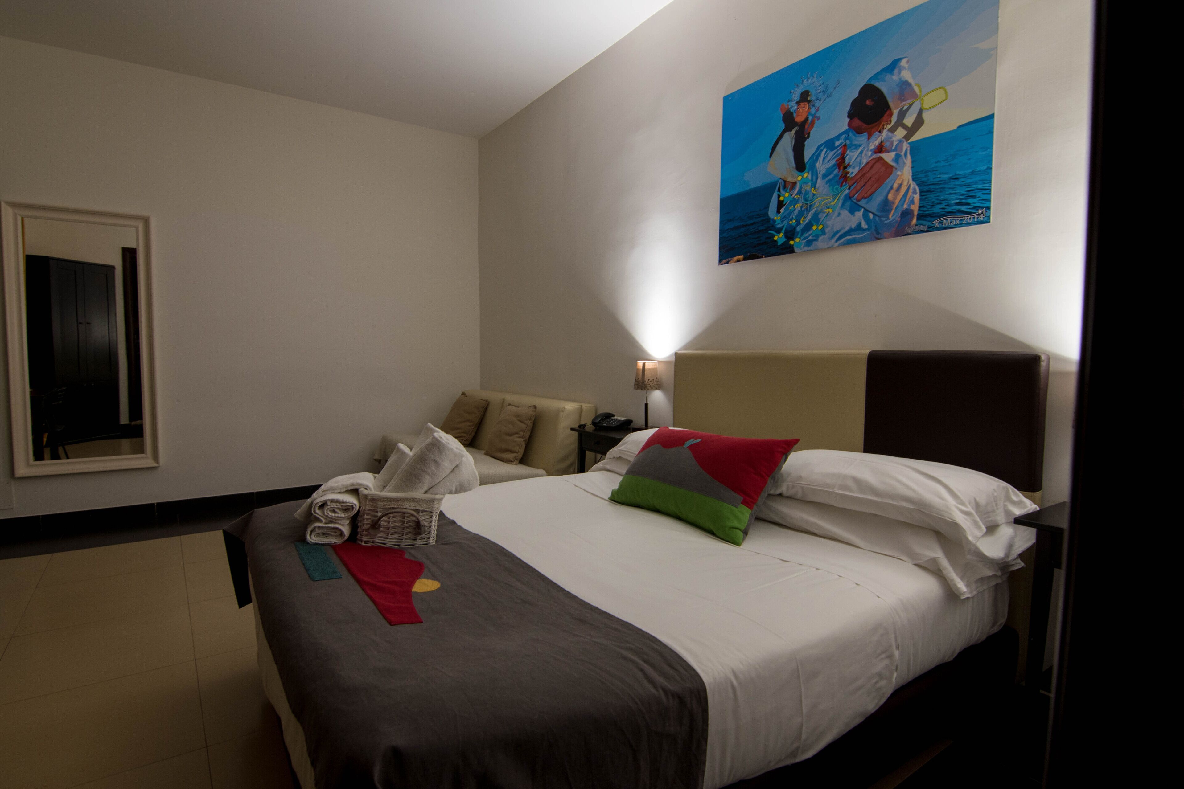 A hotel room with a bed, pillows, a nightstand, a lamp, and a painting on the wall.