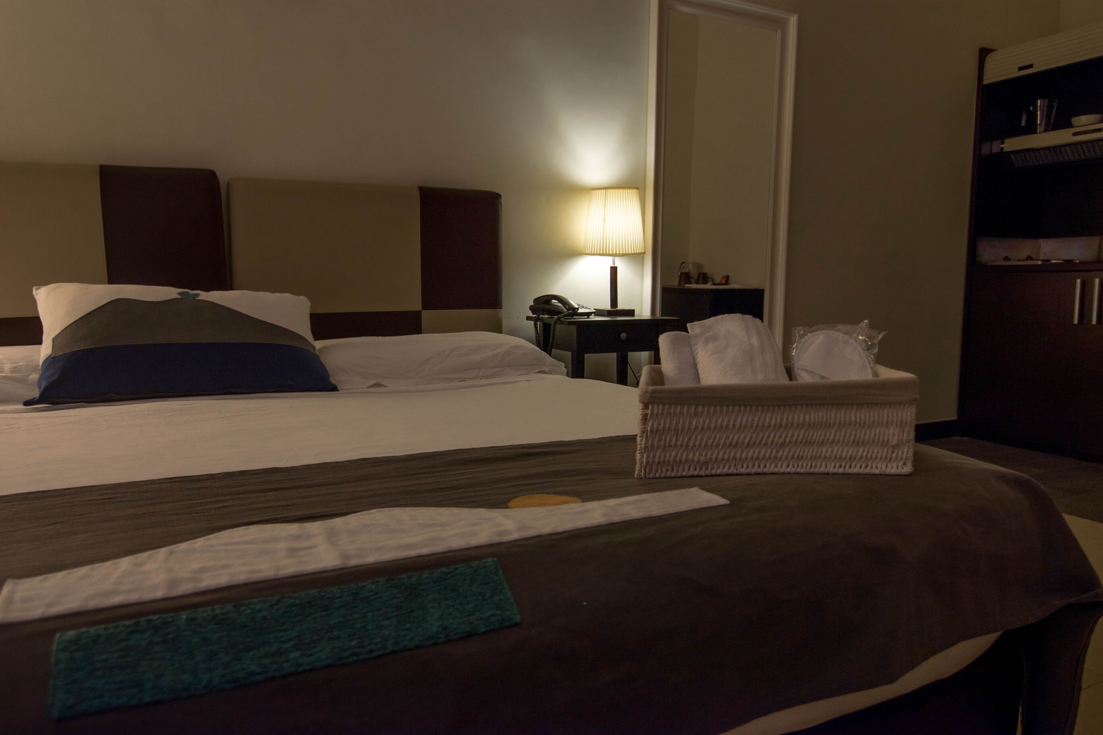 A hotel room with a bed, a nightstand, a lamp, a chair, and a wardrobe.