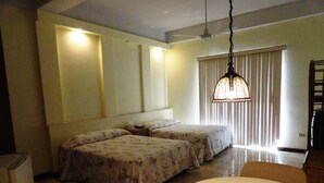 Una habitación de hotel con dos camas, una mesa redonda, un ventilador de techo y una ventana con persianas.