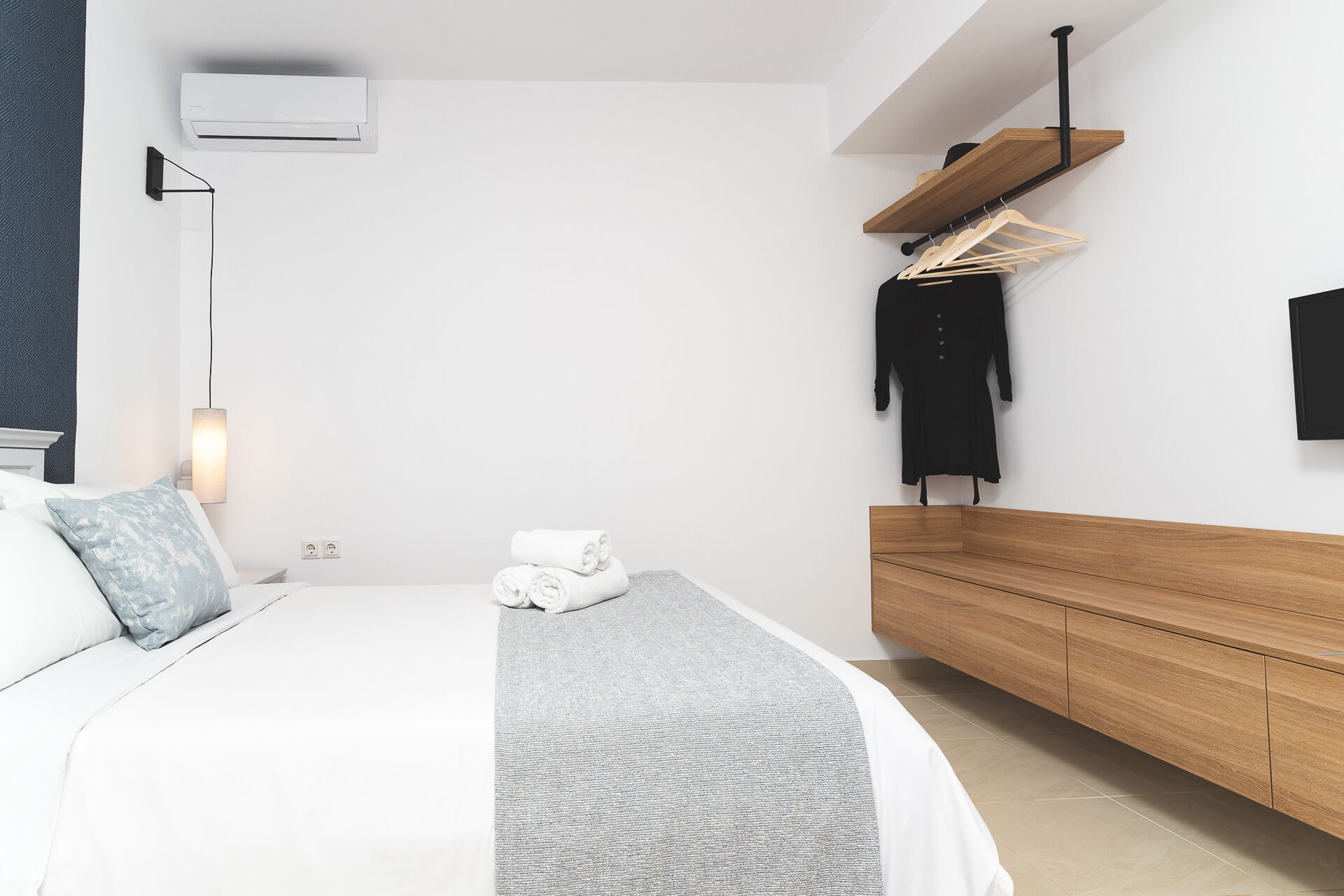 A modern bedroom with a bed, bedside table, wall-mounted air conditioner, and a wooden bench.