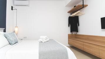 A modern bedroom with a bed, bedside table, wall-mounted air conditioner, and a wooden bench.