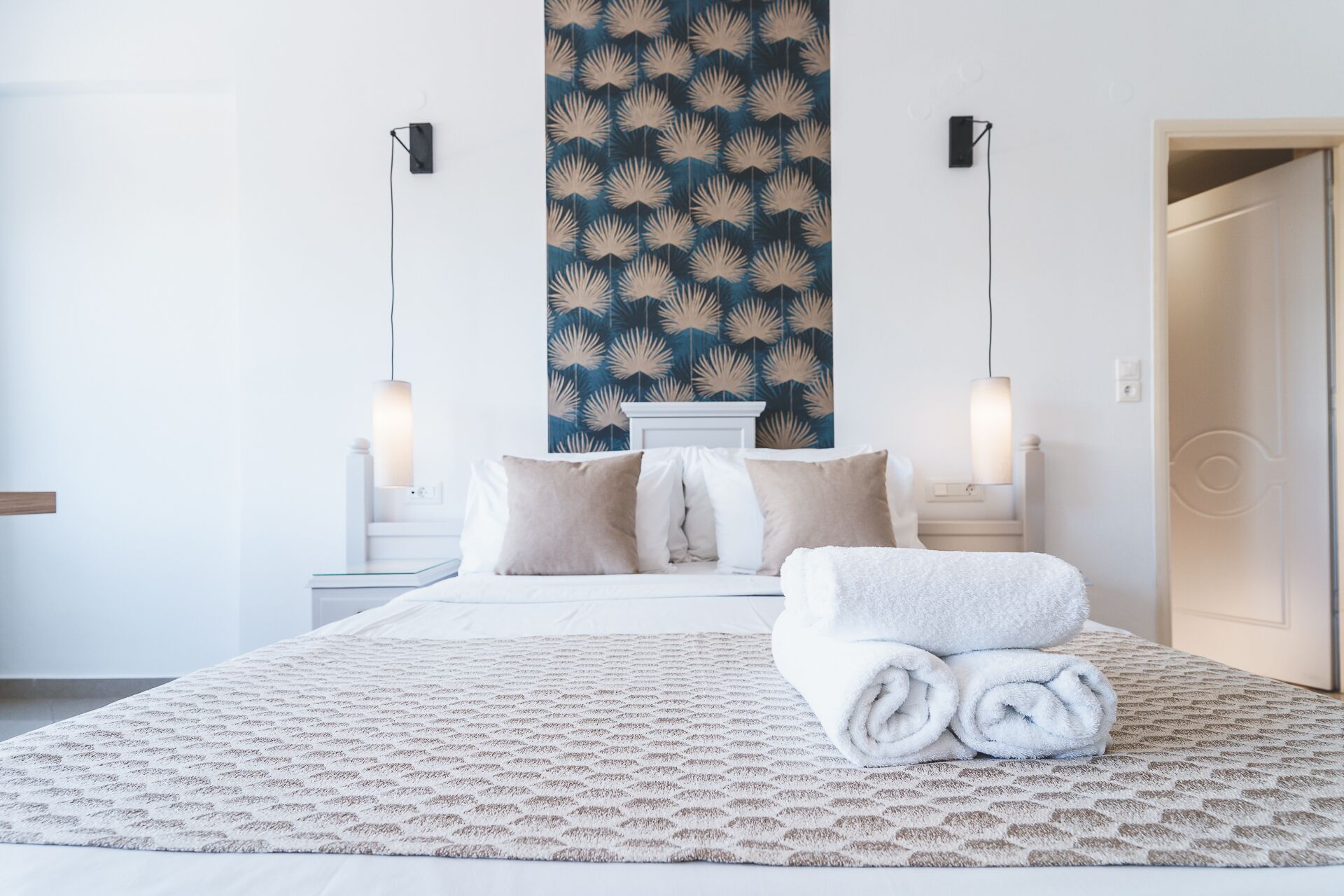 Una cama bien hecha con una colcha estampada, dos lámparas de noche y una pared con un panel decorativo.