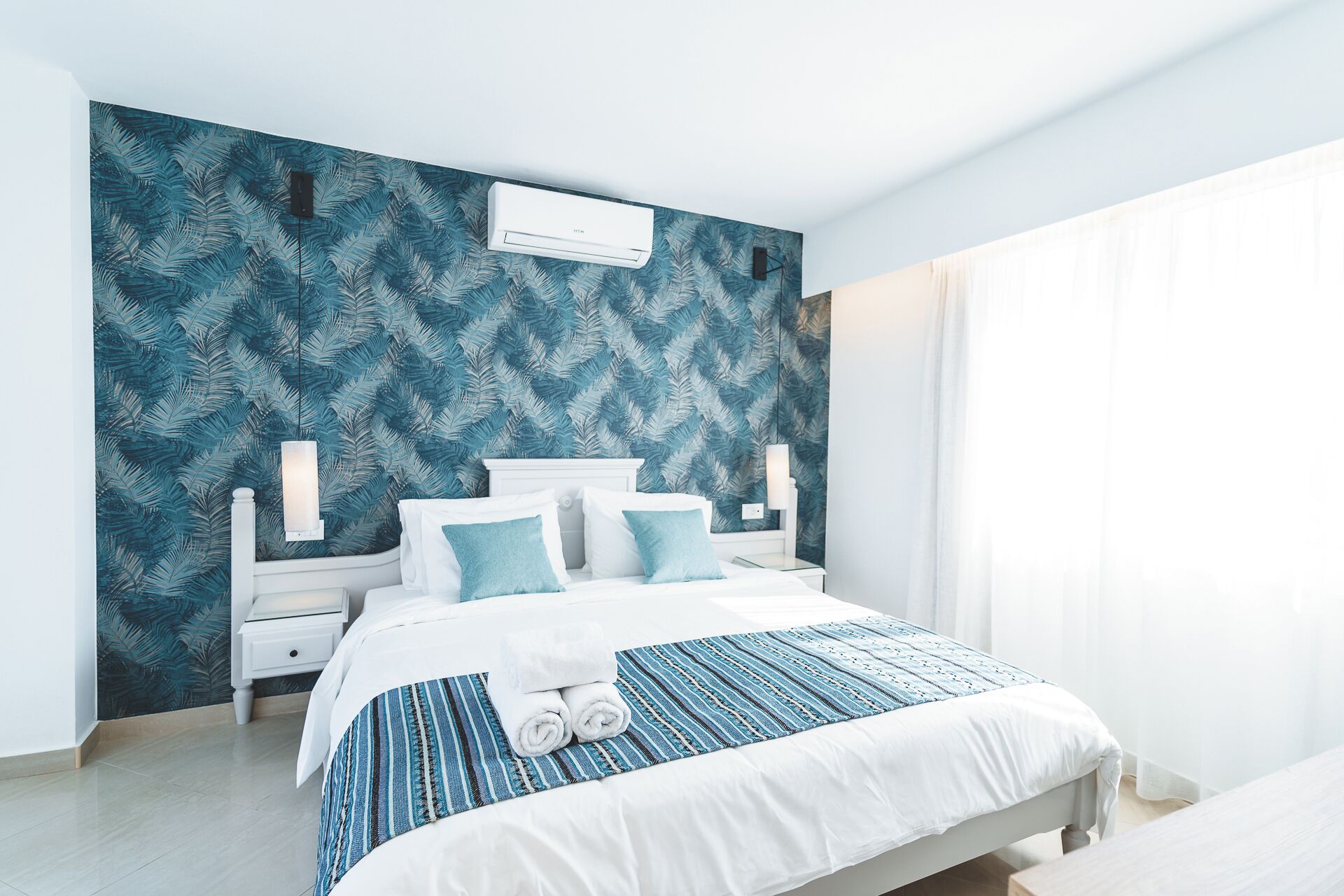 A modern bedroom with a large bed, white headboard, and a patterned wall.