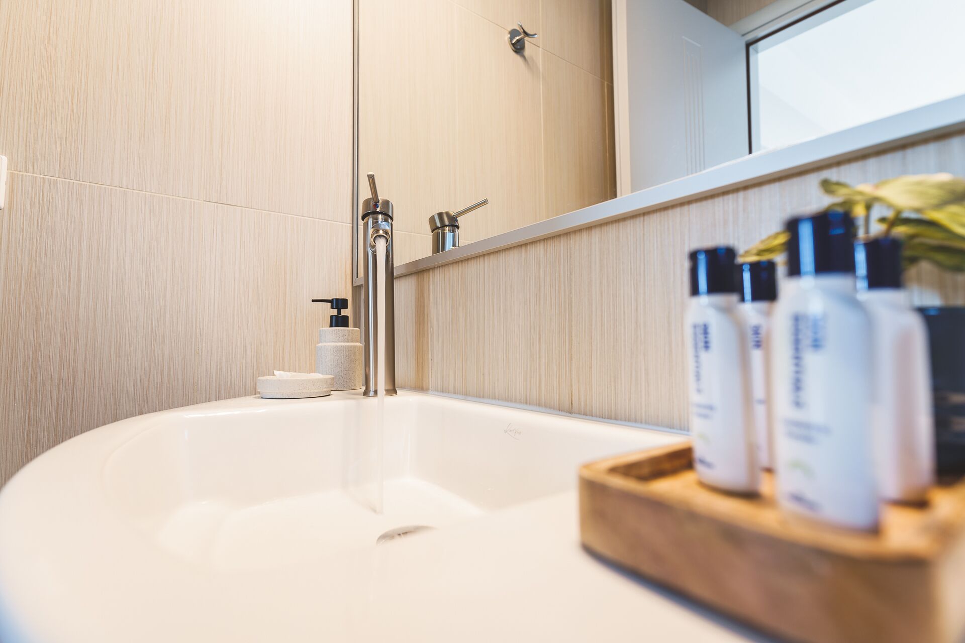 Un baño moderno con una bañera independiente, un dispensador de jabón para manos y una bandeja de madera con tres botellas de champú.