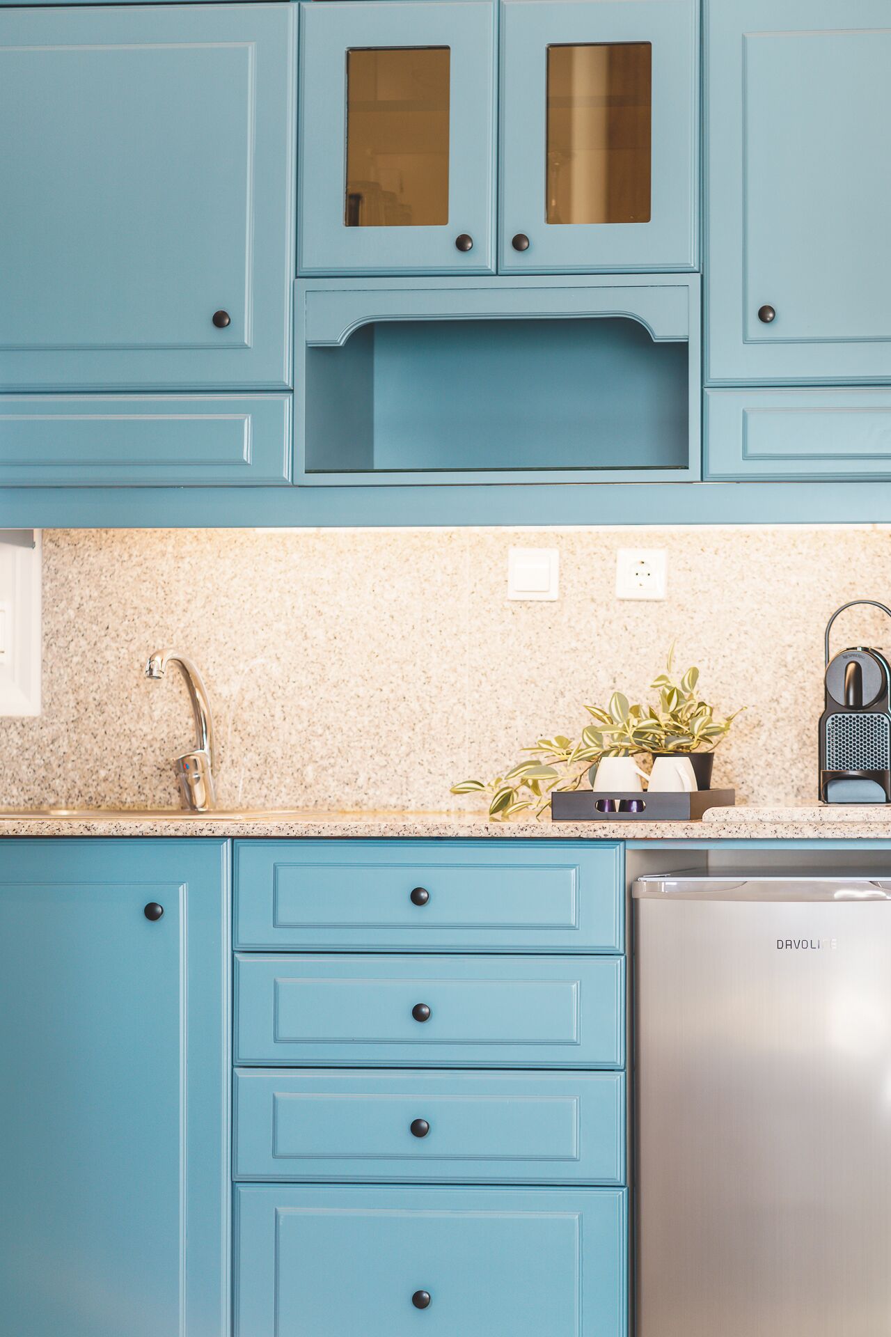 Une cuisine avec des armoires de couleur turquoise, un lave-vaisselle en acier inoxydable et un comptoir en granit.