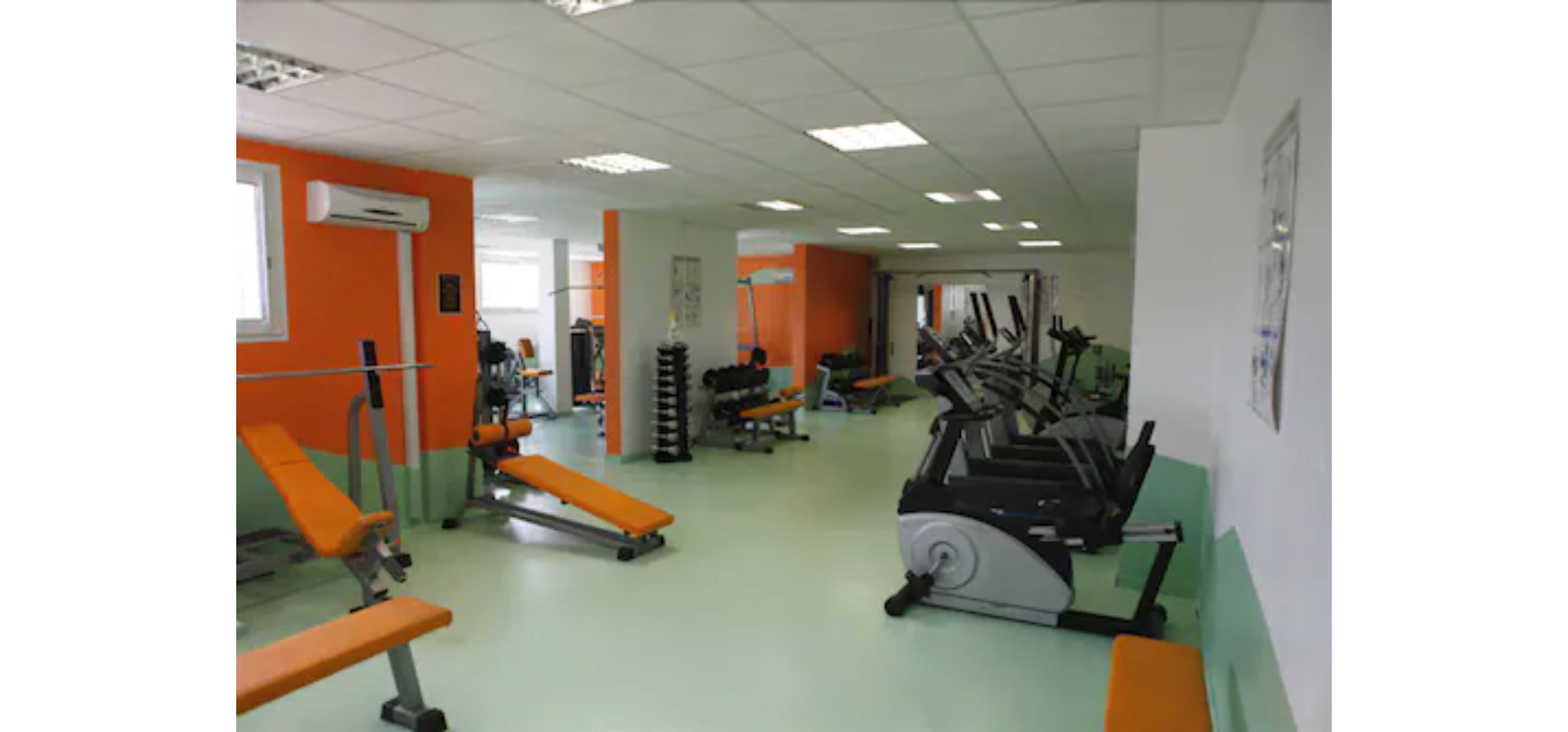 Un gimnàs amb equip d'exercici, incloent cintes de córrer i aparells de musculació.