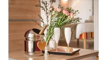 A metallic container with a heart-shaped decoration, a bouquet of flowers, and two champagne flutes on a tray.