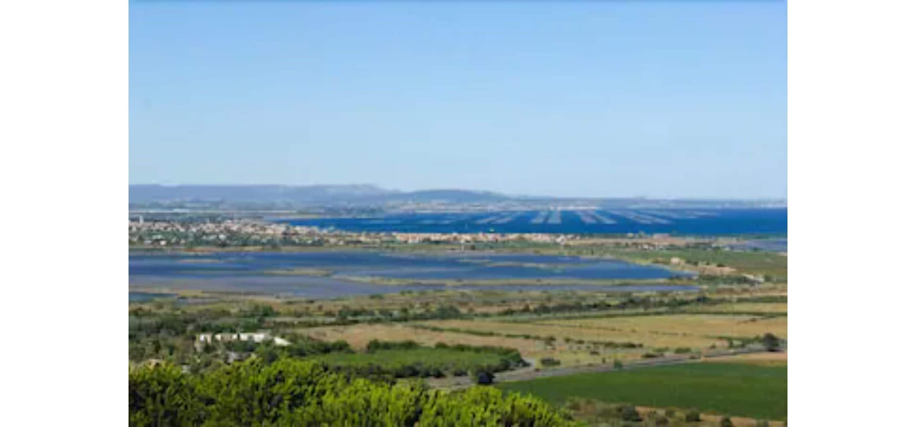 A coastal landscape with a clear sky, a body of water, and distant buildings.