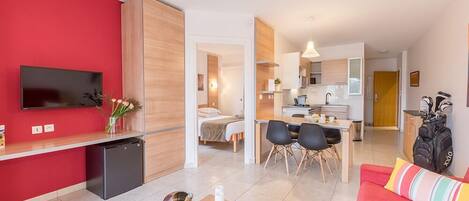 A modern apartment with a red accent wall, a kitchen, a dining area, and a living room with a TV and a small fridge.