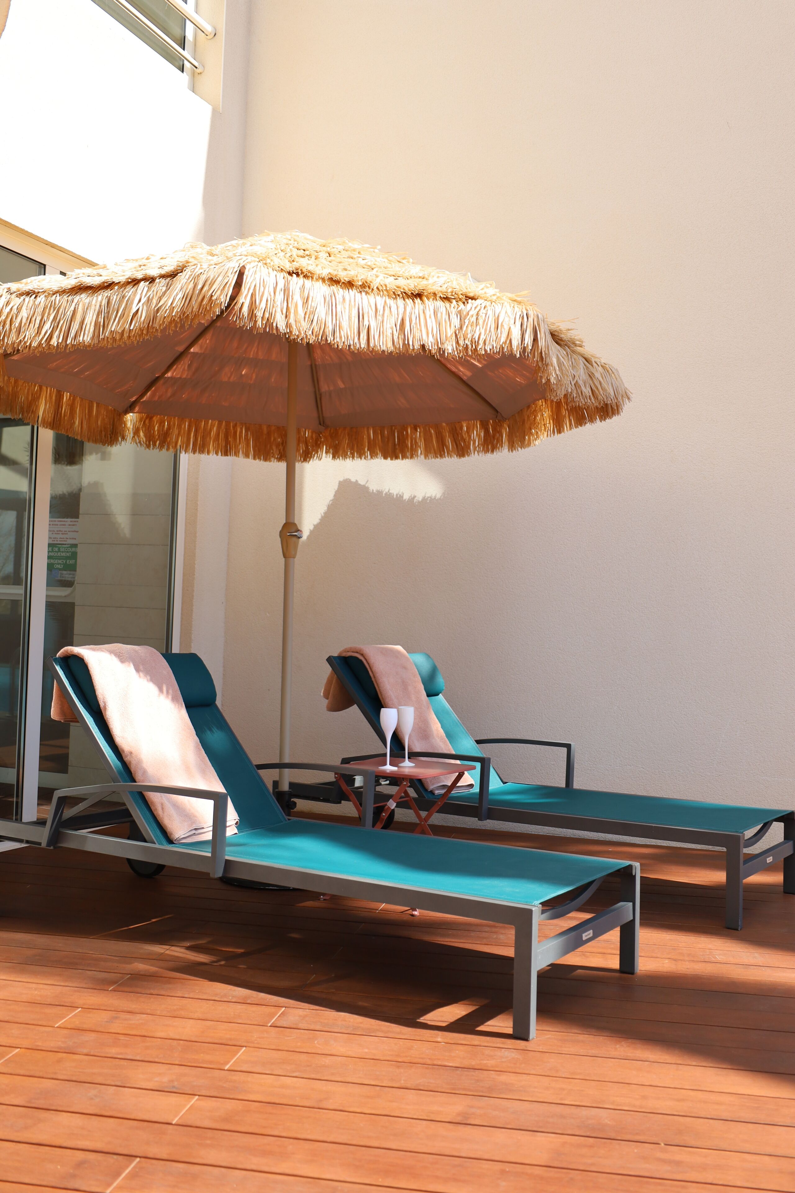 A sunlit outdoor seating area with two lounge chairs and a thatched umbrella.