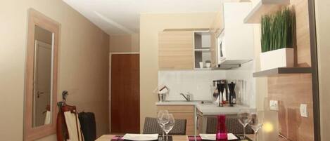 Un coin repas avec une table dressée pour quatre personnes, une cuisine en arrière-plan et une porte sur la gauche.