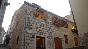 A stone building with wooden shutters, a visible staircase, and a sign indicating a business. - Apartments Santa Maria (Dubrovnik)