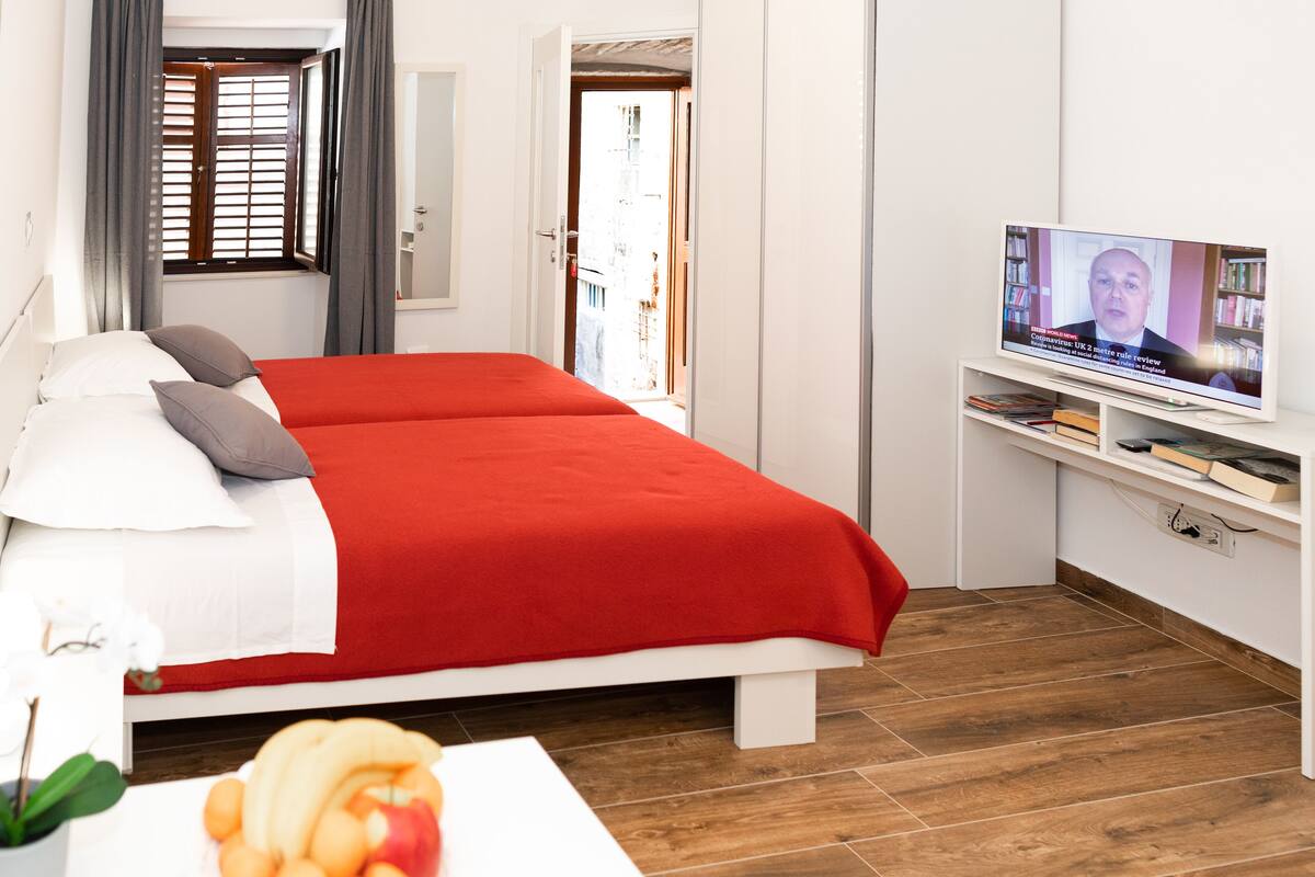 Una habitación de hotel con cama, televisión y una pequeña mesa con fruta.