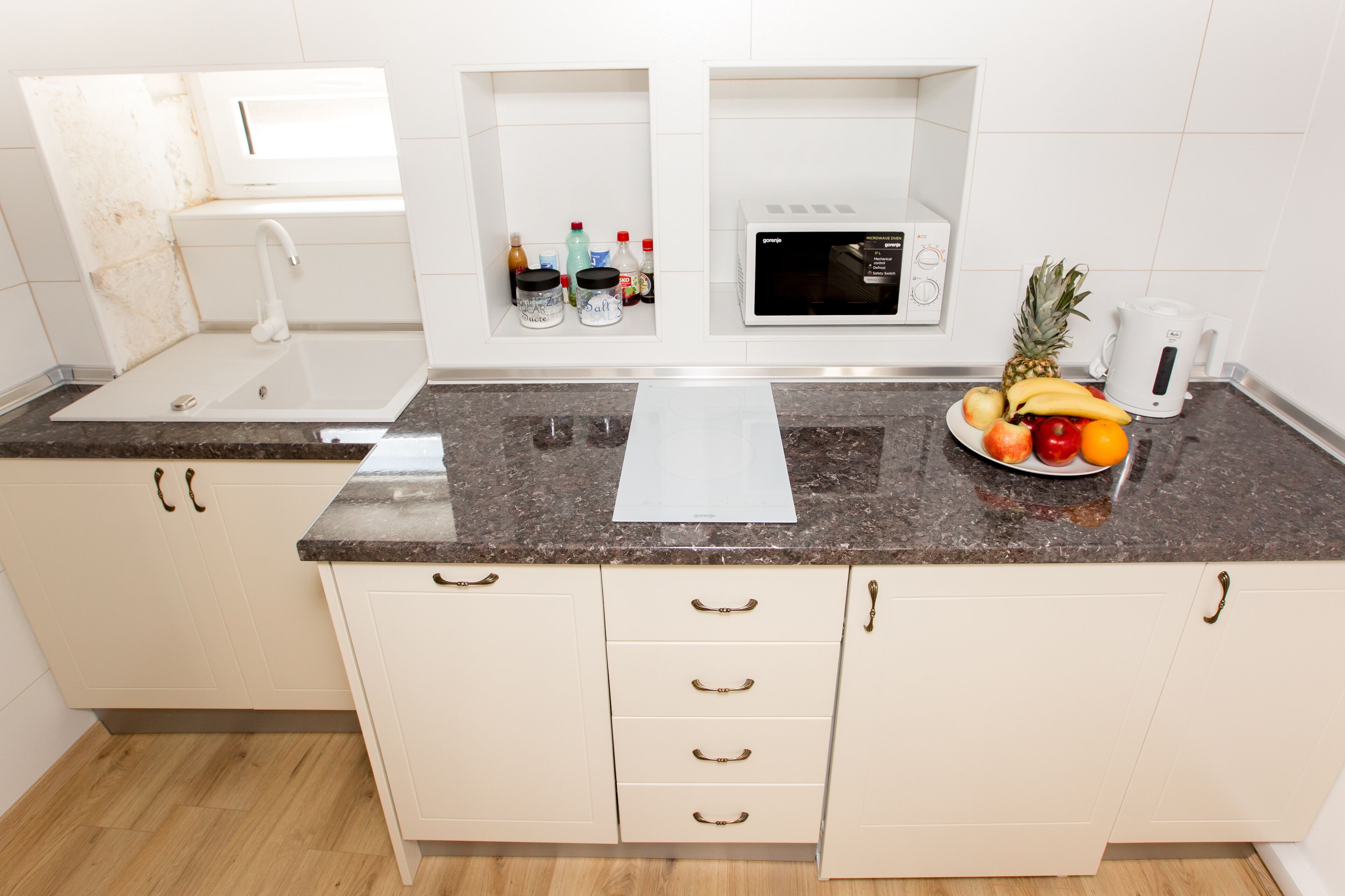 Een keuken met witte kastjes, een granieten aanrecht, een magnetron en een schaal fruit.