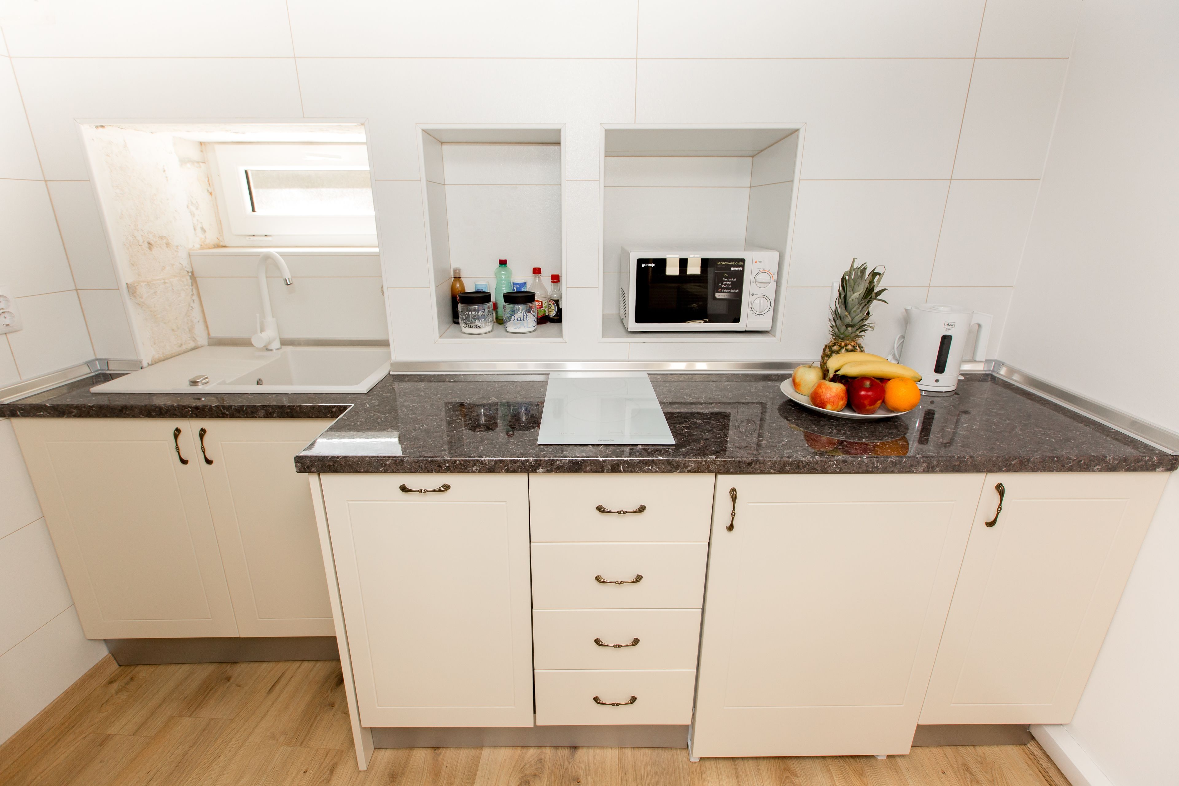 A kitchen with white cabinets, a granite countertop, a microwave, a sink, and a fruit bowl.
