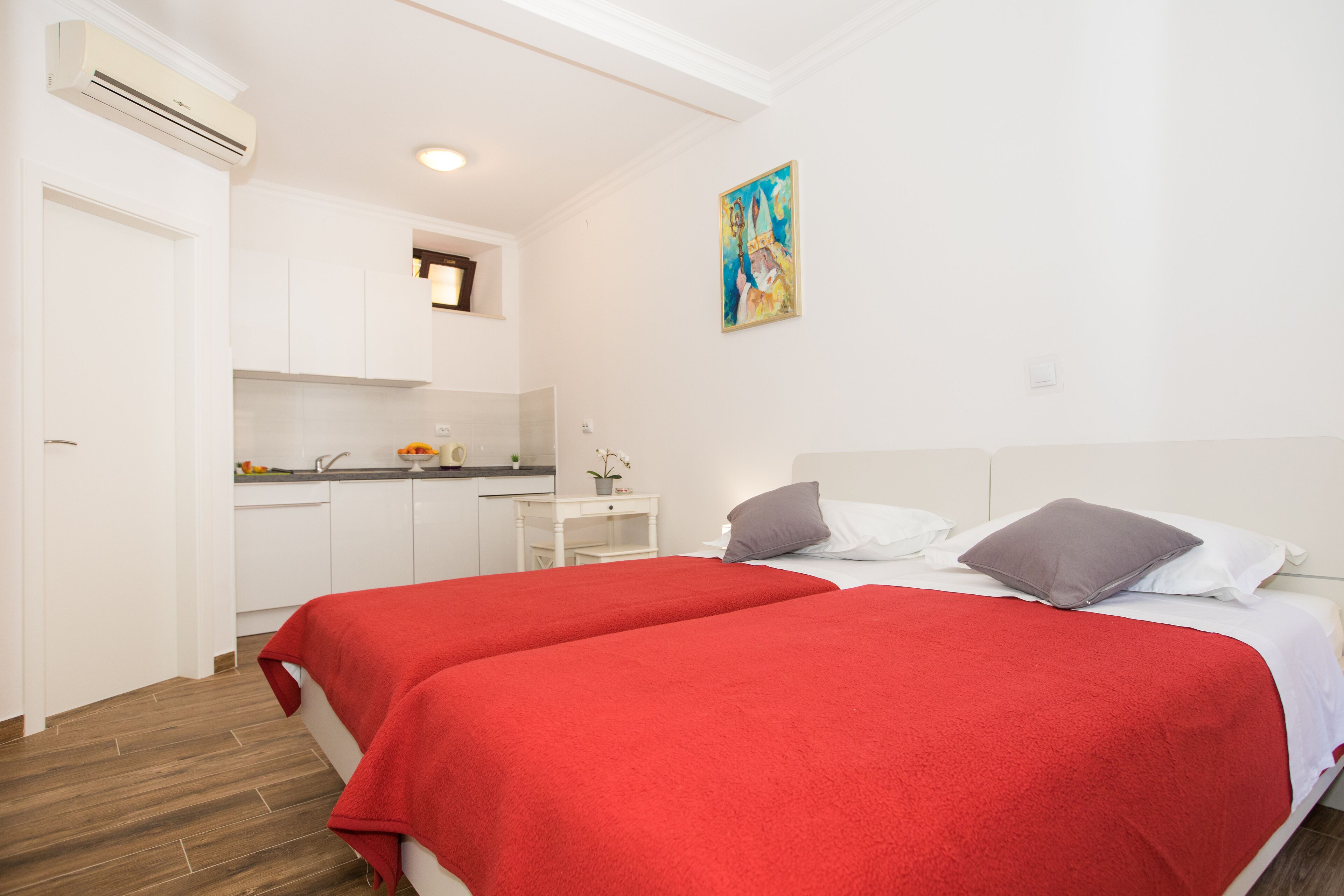 A bedroom with two beds, a kitchenette, and a painting on the wall.