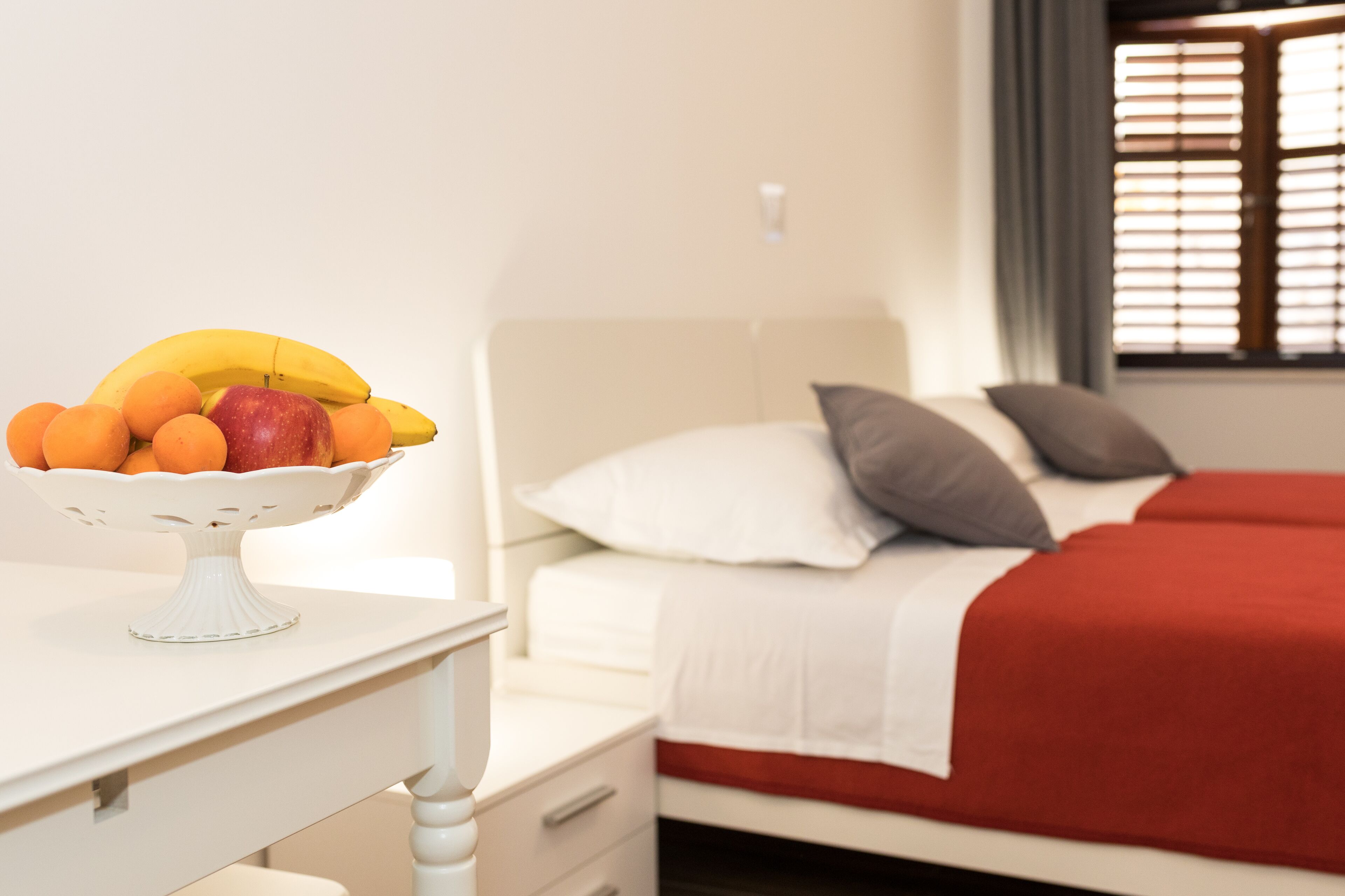A bed with a red blanket, white pillows, and a white headboard.