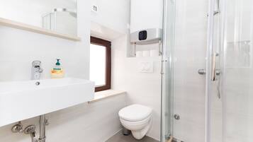 A modern bathroom with a white sink, a toilet, a glass shower enclosure, and a window above the sink.