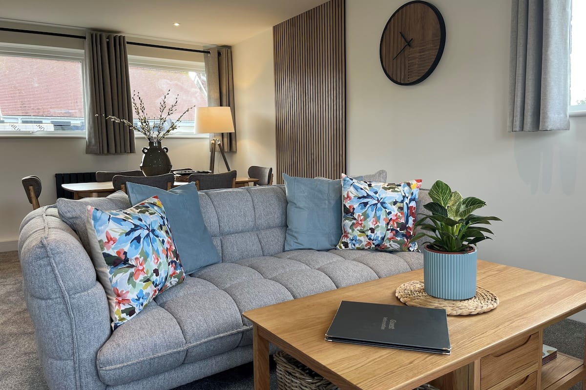 A modern living room with a grey sectional sofa, a wooden coffee table, a laptop, and a potted plant.