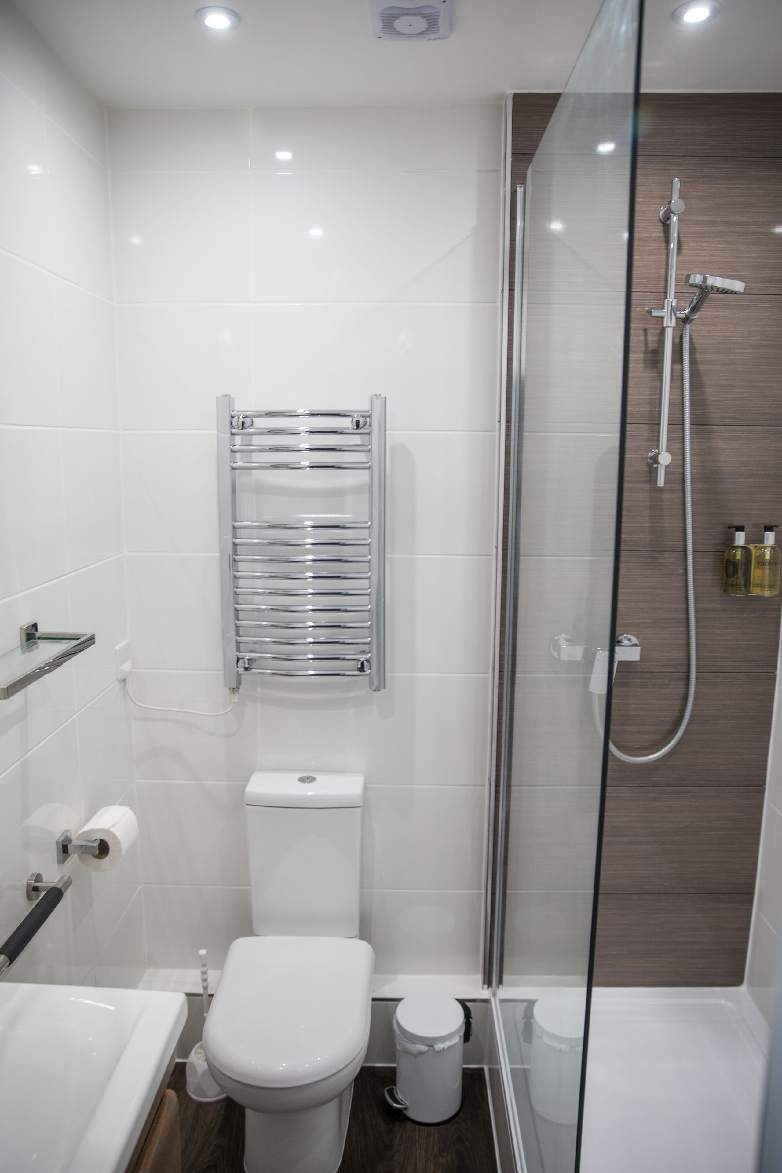 A modern bathroom with a glass-enclosed shower, a white toilet, and a chrome towel rack.
