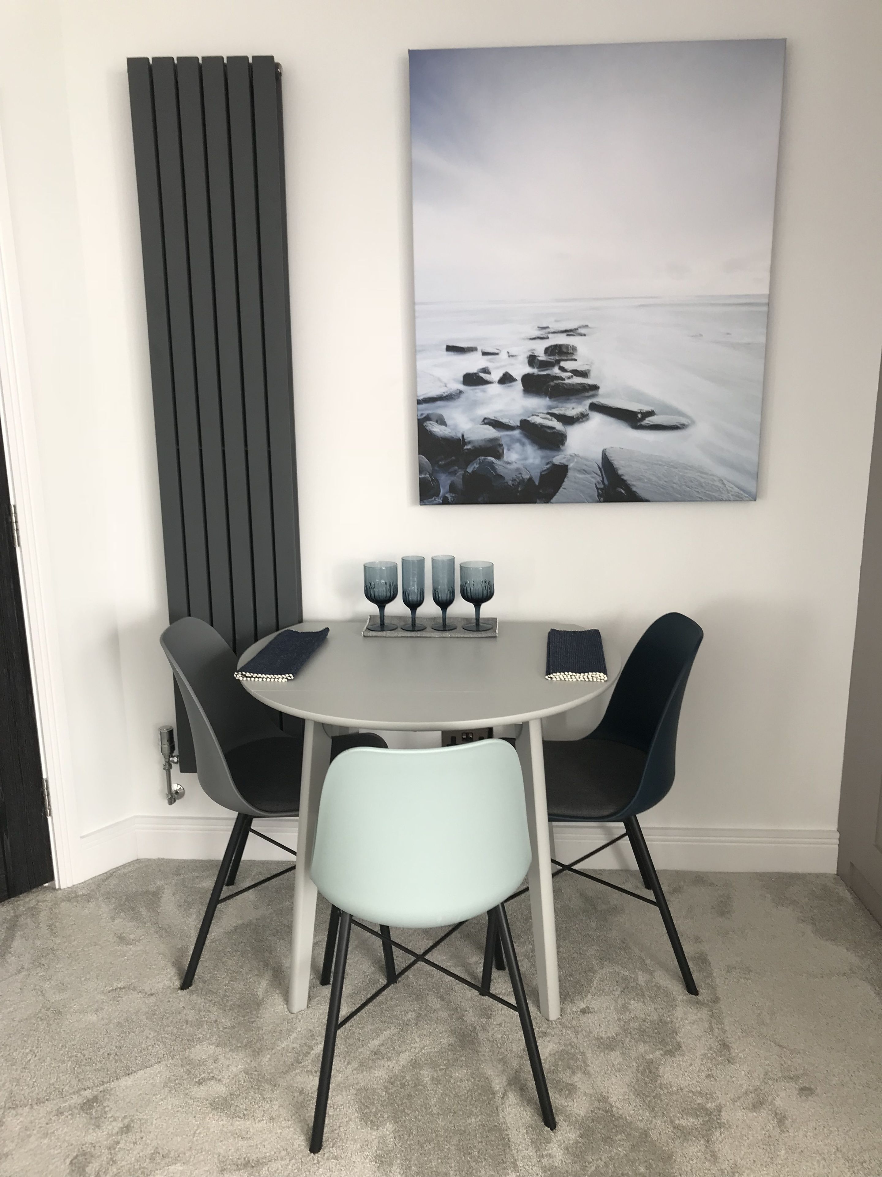 A dining area with a round table, two black chairs, and a light blue chair. There are four wine glasses on the table.