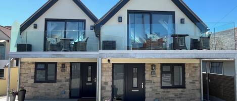 Una casa moderna de dos pisos con balcón, fachada de piedra y ventanas amplias.