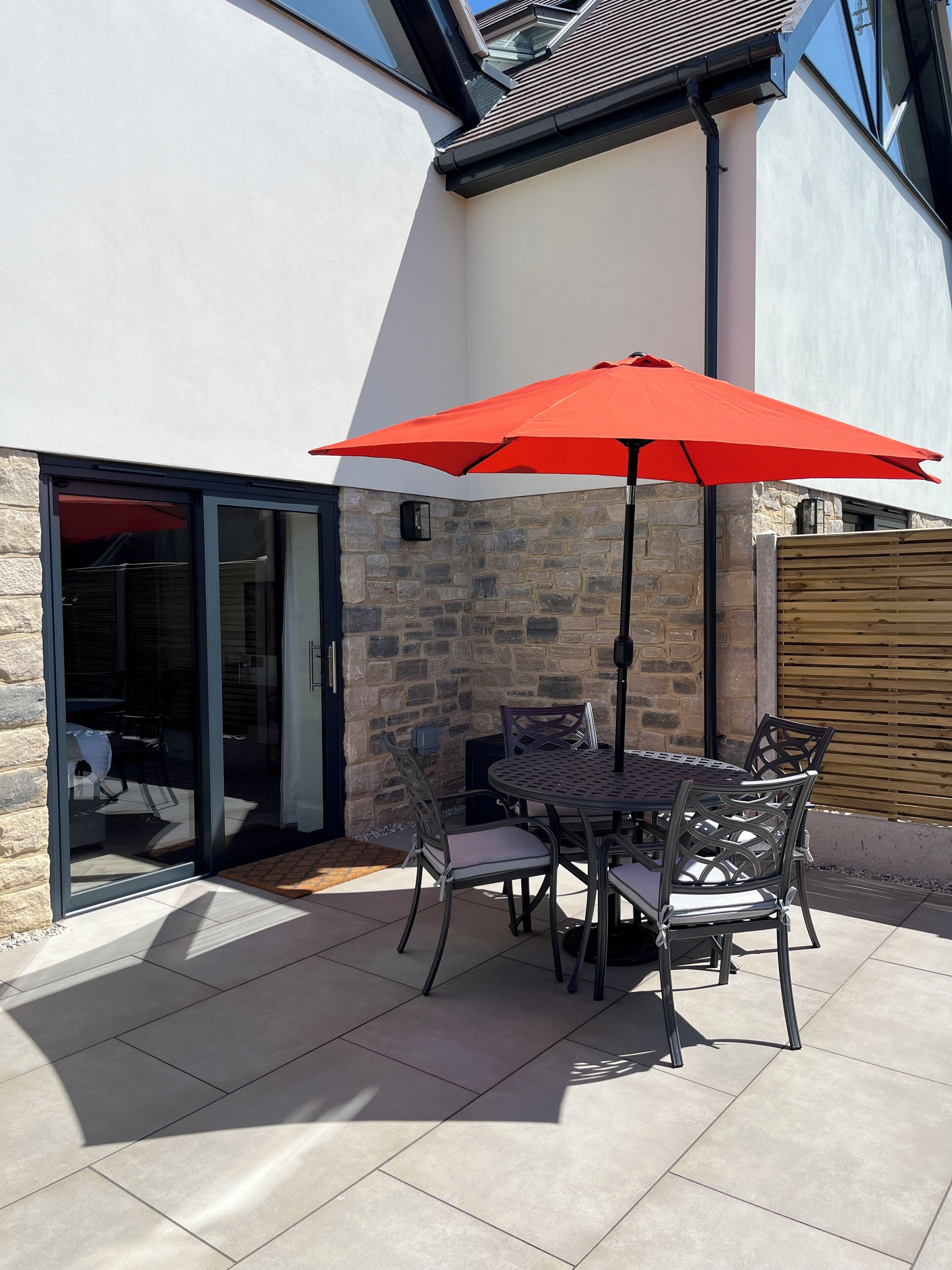 A patio with a table and chairs, a red umbrella, and a stone wall.