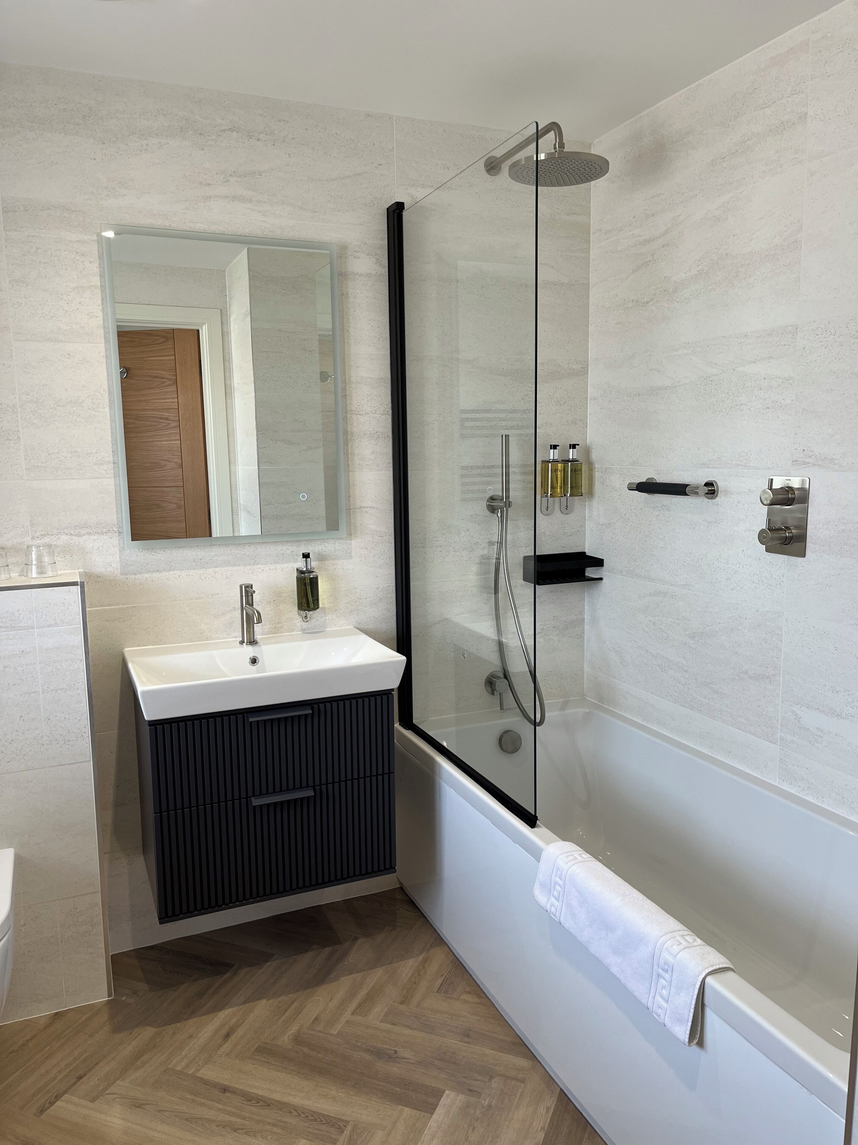 A modern bathroom with a glass-enclosed shower, a white sink with a black vanity, and a wooden door.