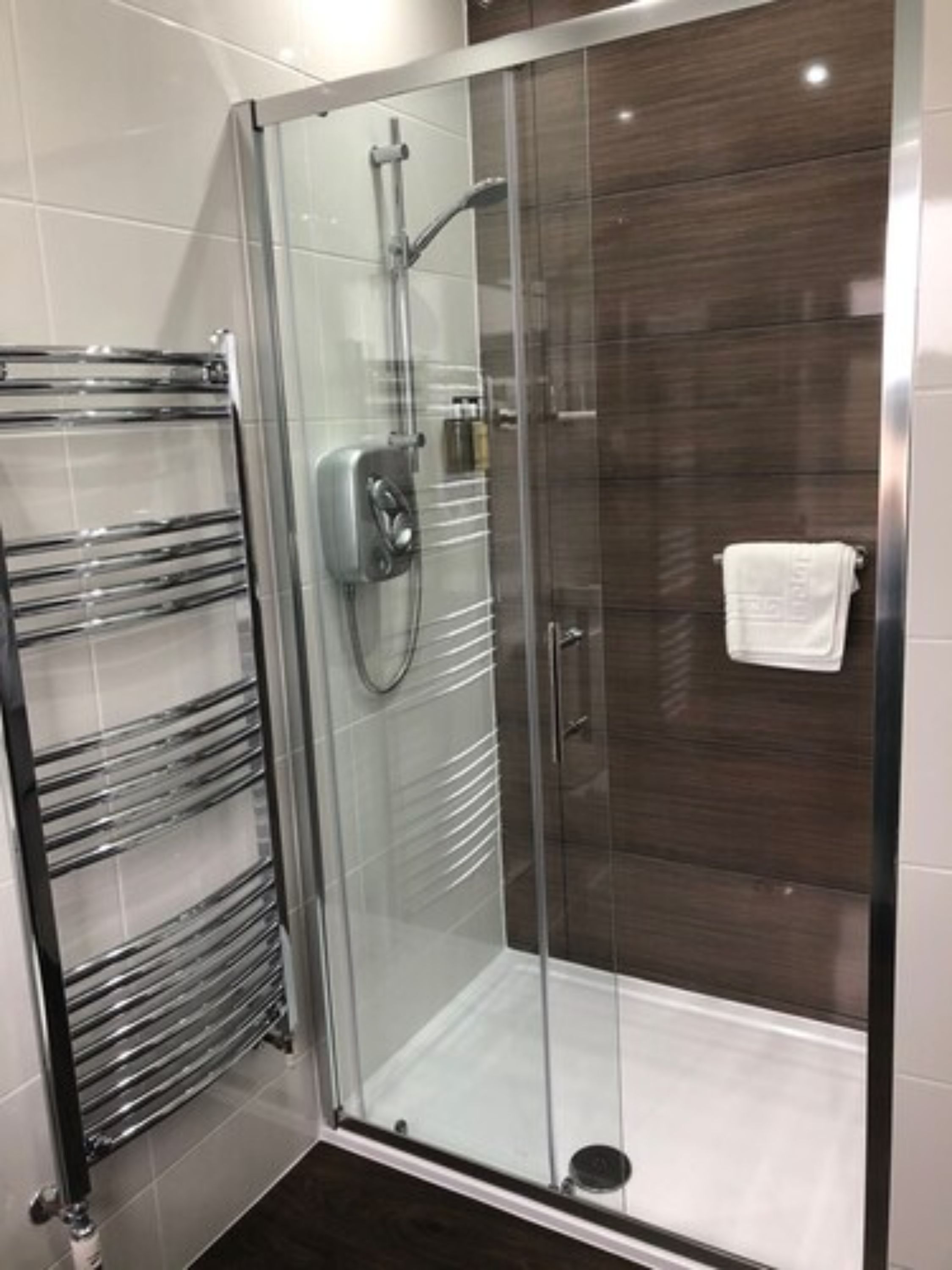 A glass-enclosed shower with a chrome towel rack and a white towel hanging on the wall.