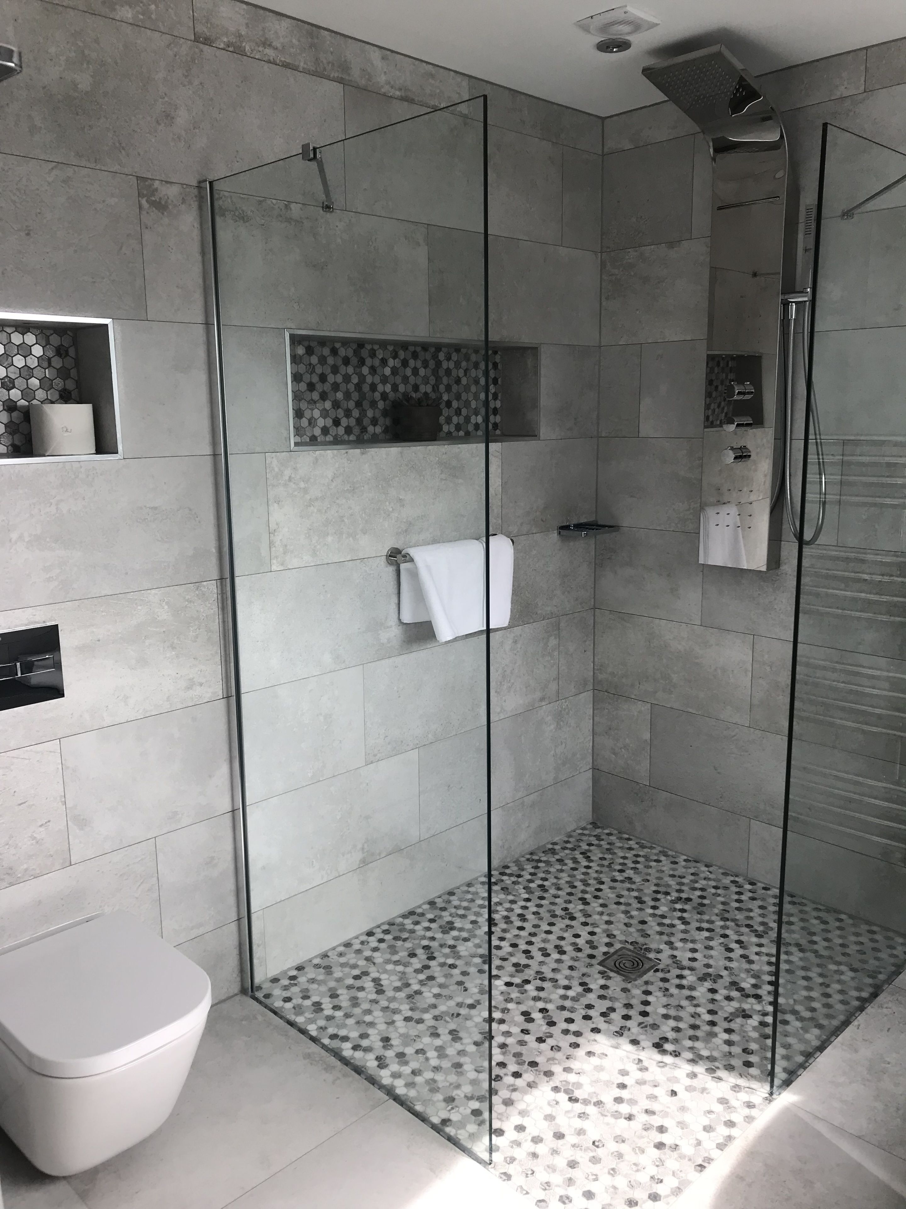 Un baño moderno con ducha de vidrio, inodoro y piso estampado.