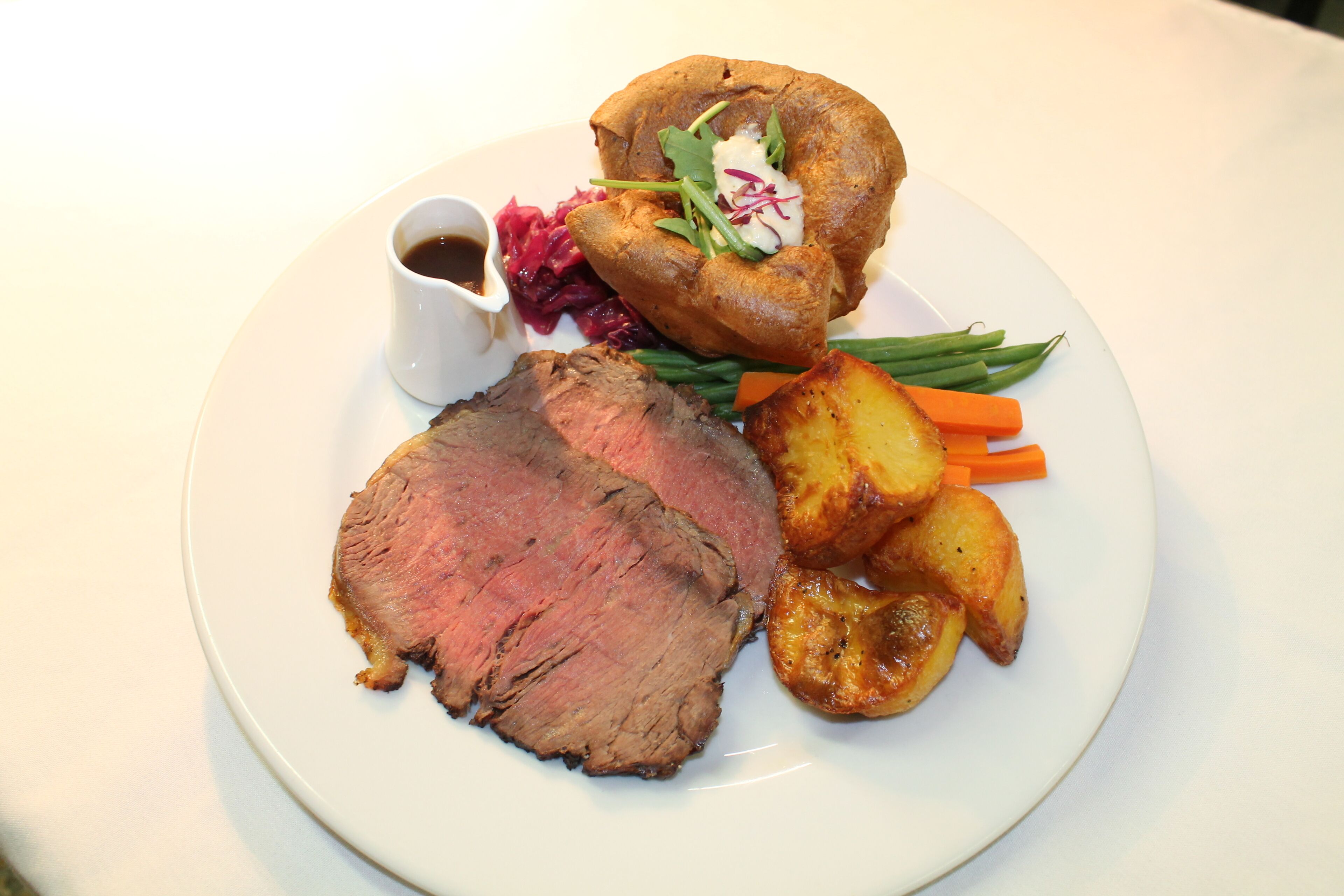 A plate with roast beef, Yorkshire pudding, roasted potatoes, green beans, and red cabbage.