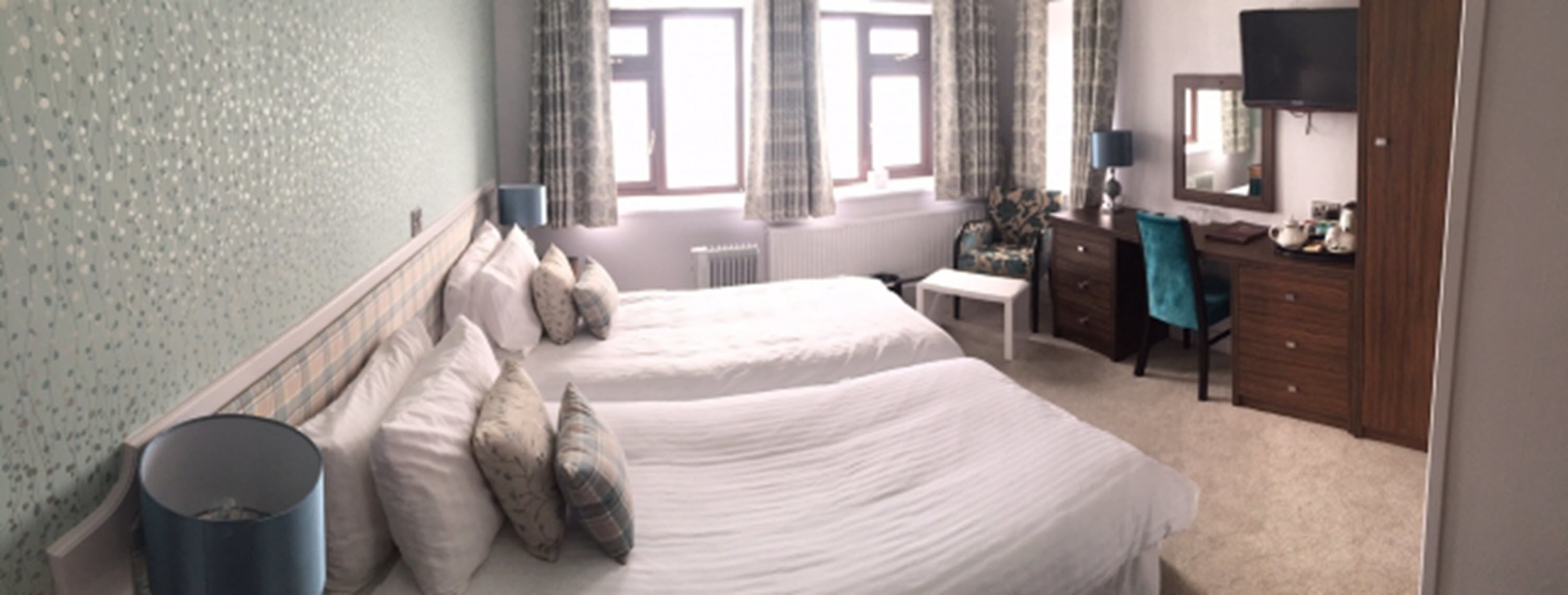 A hotel room with two beds, a desk, a chair, a dresser, and a TV.