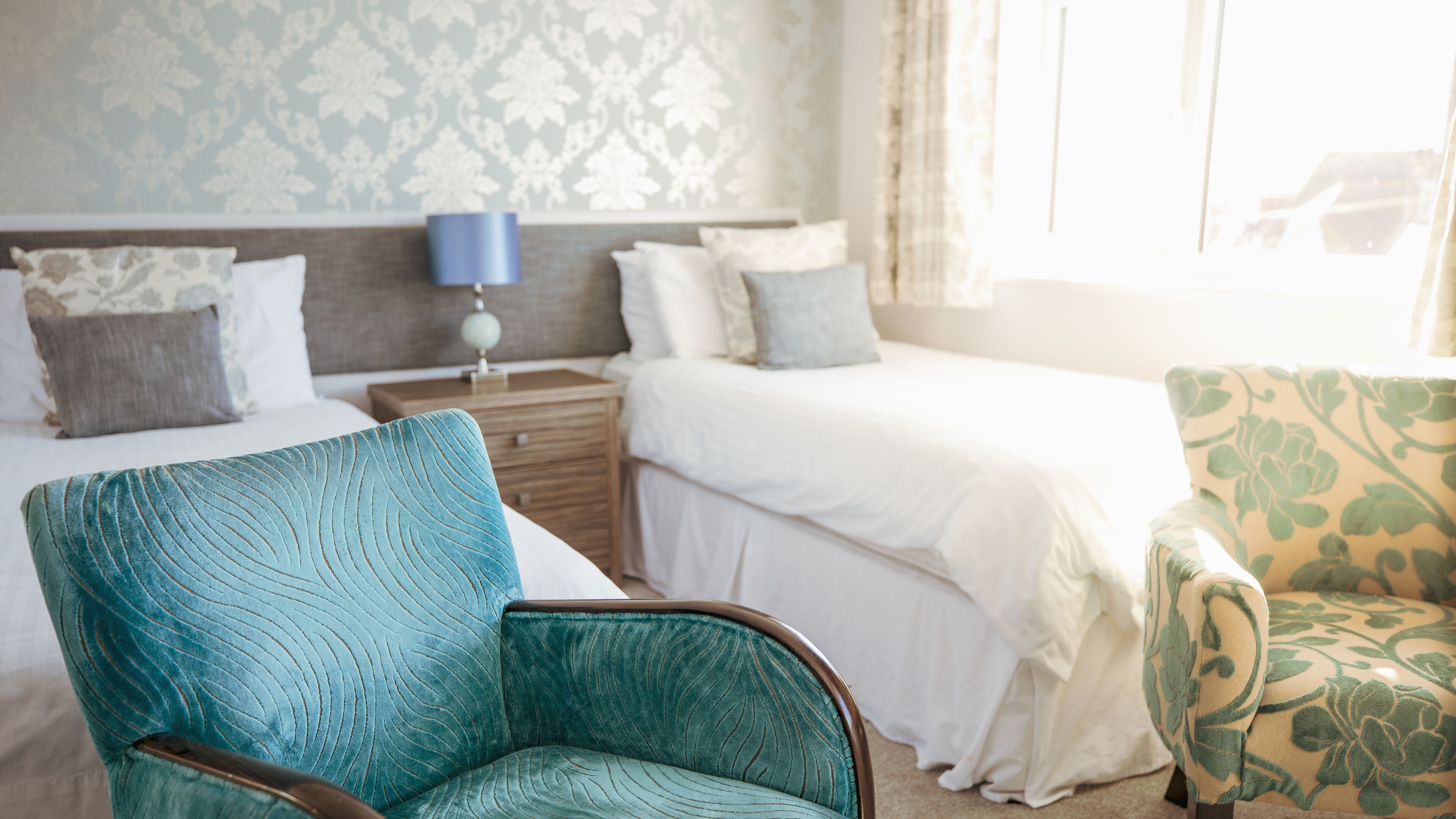 Une chambre d’hôtel avec un lit, une chaise, une table de chevet et une lampe.