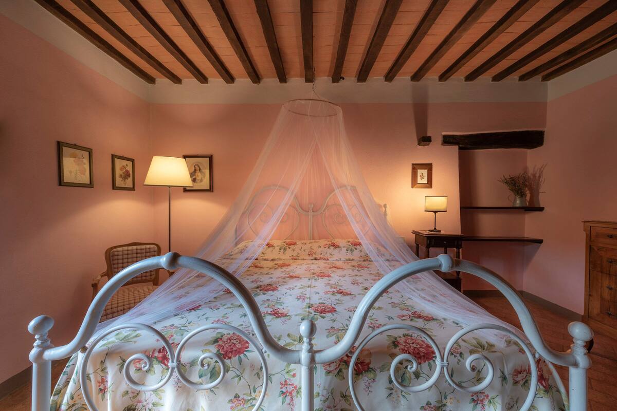 A bedroom with a canopy bed, floral bedding, and a wooden ceiling.