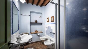 Een badkamer met een wastafel, twee kommen, een toilet en een bidet. Boven het toilet bevindt zich een plank en aan de muur hangt een spiegel.