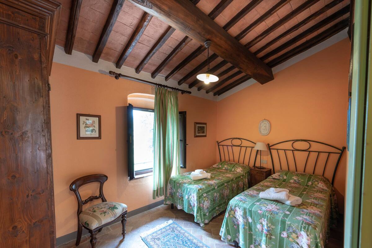 A bedroom with two single beds, a wooden chair, a window with curtains, and a bed with a towel.