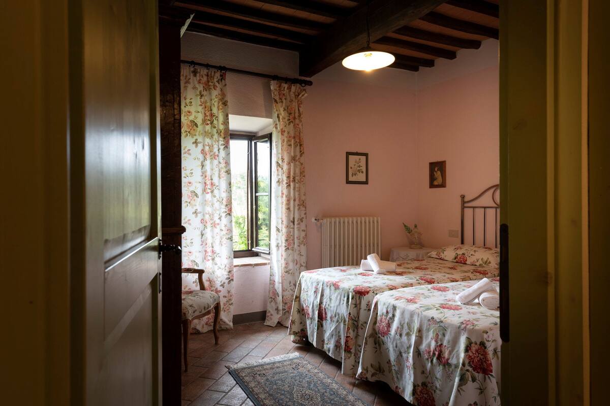 A bedroom with a bed, a chair, a window with curtains, a radiator, and a picture on the wall.