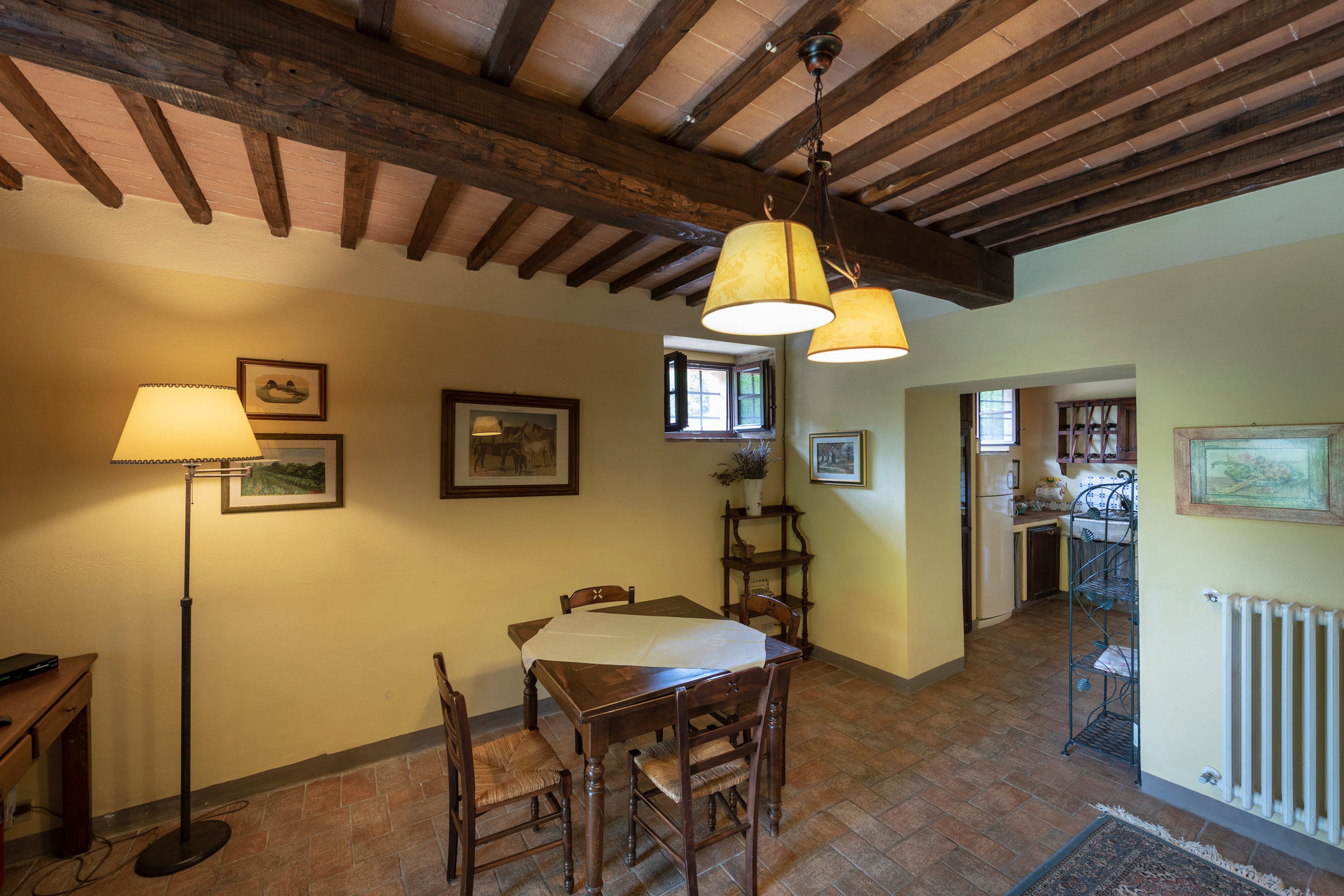 A dining area with a wooden table and chairs, a floor lamp, and a ceiling with exposed beams.