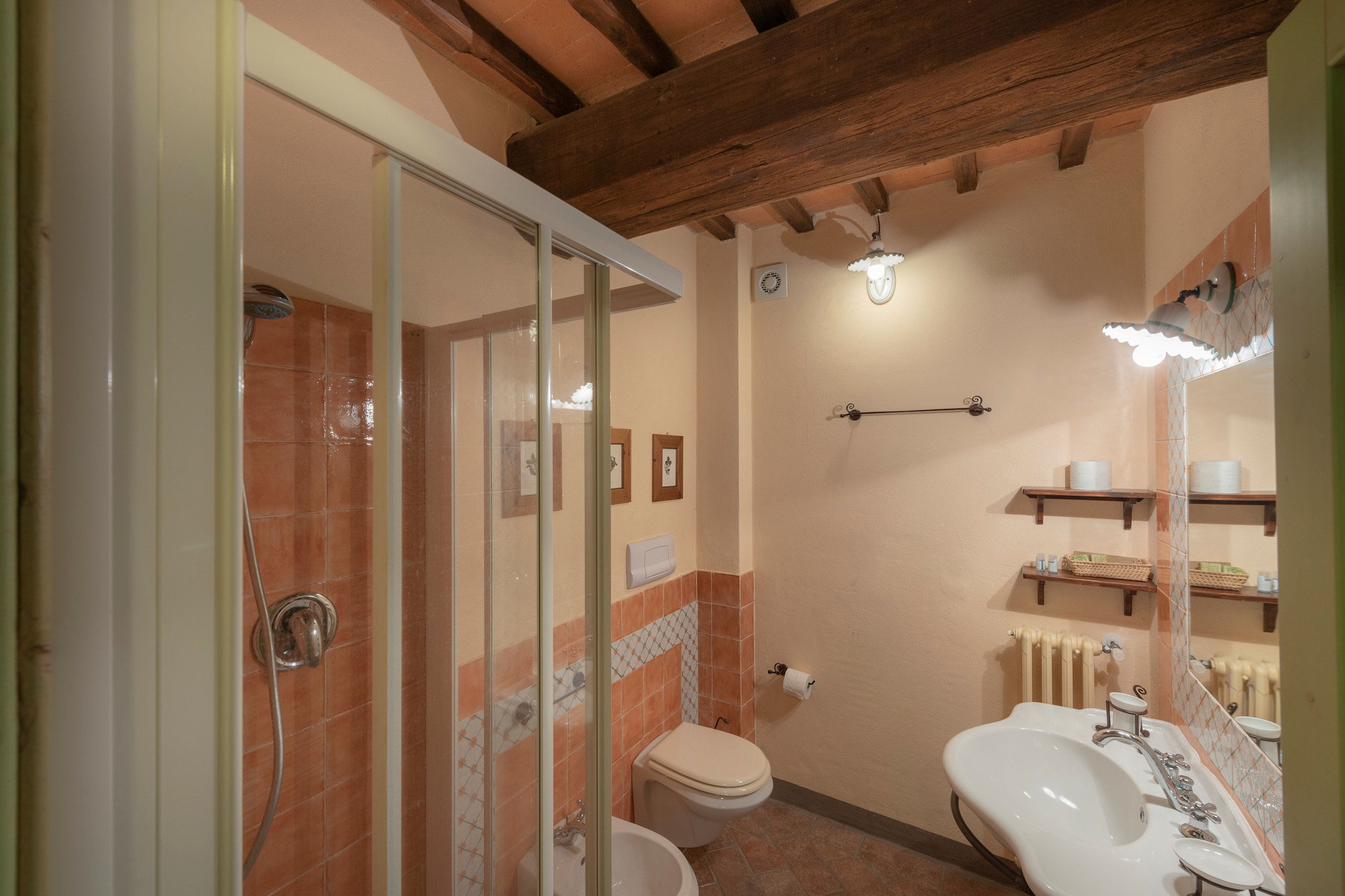 Ein Badezimmer mit Dusche, Toilette und Waschbecken, mit Holzbalken an der Decke und gefliesten Wänden.