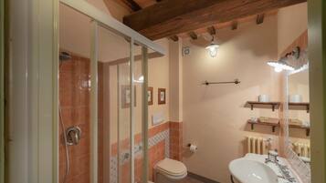 Ein Badezimmer mit Dusche, Toilette und Waschbecken, mit Holzbalken an der Decke und gefliesten Wänden.