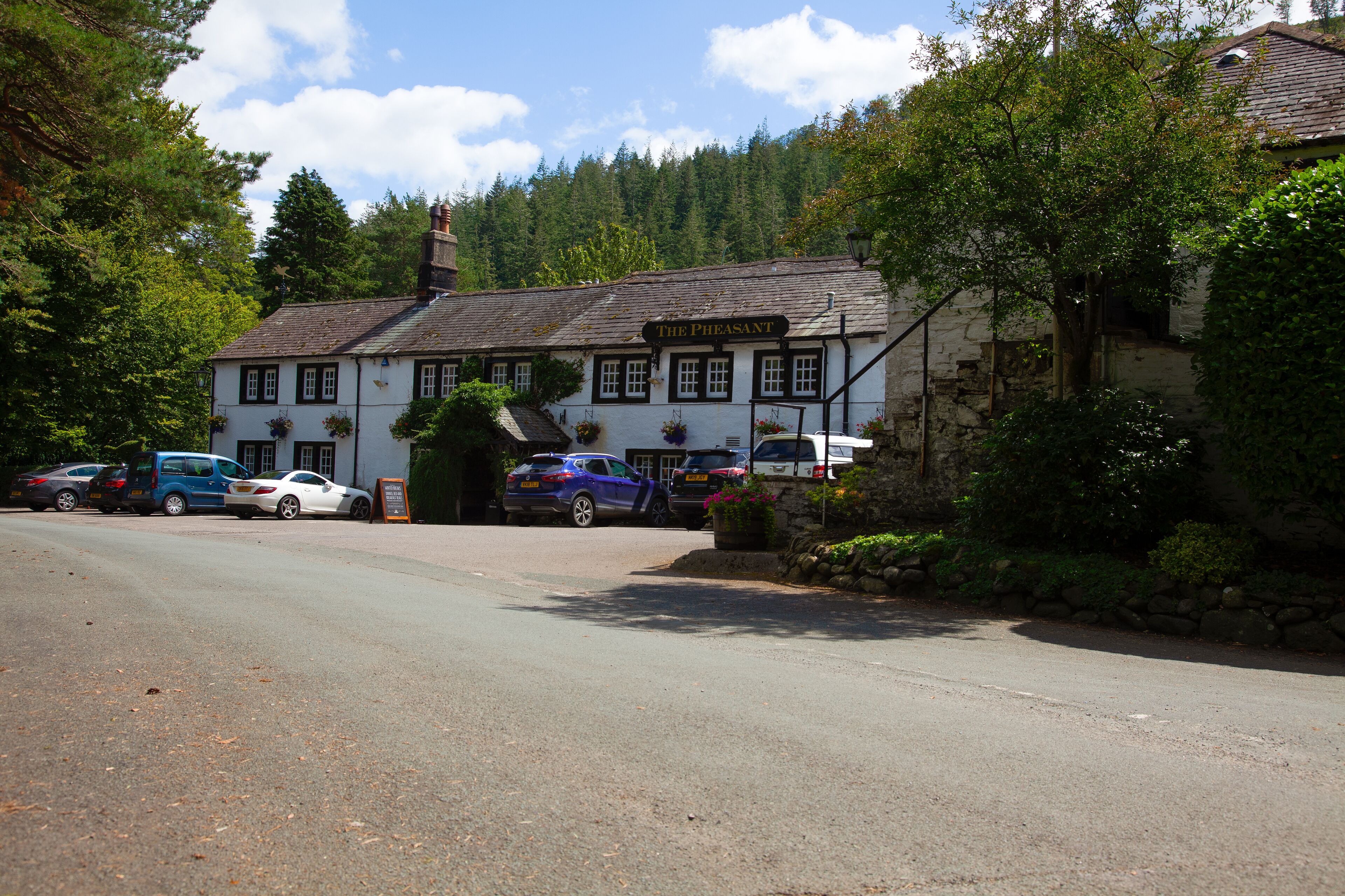 A traditional white building with a sign reading "The Pheasant." There are parked cars in front, and the building is surrounded by trees.