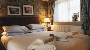 A neatly made bed with pillows, a lamp, and towels on a wall with framed pictures.
