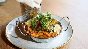 A bowl of soup with vegetables and herbs on a plate.