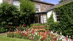 A garden with a bench, a stone building with multiple windows, and a variety of colorful flowers. - The Pheasant Inn - The Inn Collection Group (Cockermouth)